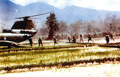 An extraction under fire. Probably a recon team, 9 or so members with very light packs. Squad leader is inside the aeroplane, at the top of the ramp. Both he and his deputy at the bottom of the ramp, are counting the men on board to make sure everyone gets on. Note the 2 guys on the top of the dyke, facing the rear. The one on the left of the picture is firing his M-16, from the hip. His boot camp drill sergeant would not like that; too John Wayne. Aircraft on ground - less than 45 seconds, we tried for 30 seconds but rarely made it. When you are just sitting there, waiting for the rounds to start hitting, every second seems like an hour. When the last guy was about 10 meters away, the crew chief would signal to the pilot to start pulling power. The last guy, who was at a dead run and filled with adrenaline, would actually have to jump to get on. Nobody ever got left behind though. Copyright TOM MIX